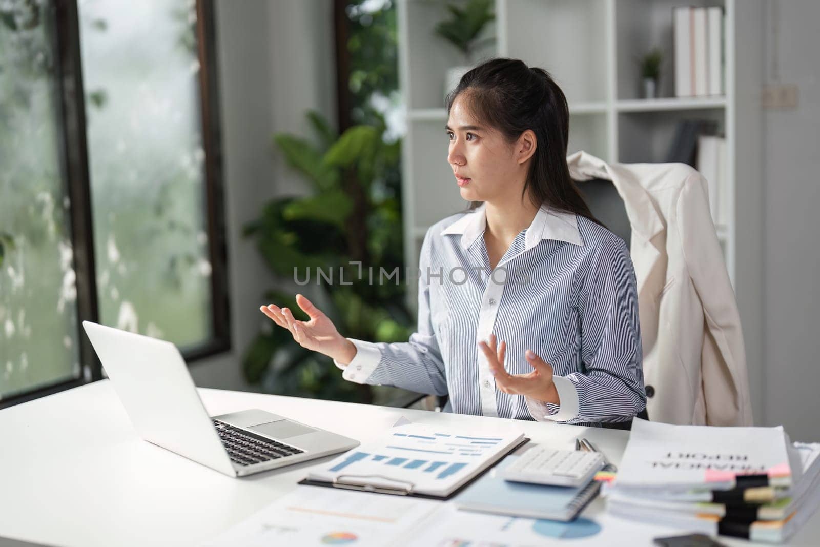 A finance professional gestures while discussing strategies during a video call, emphasizing communication and collaboration in a bright office.