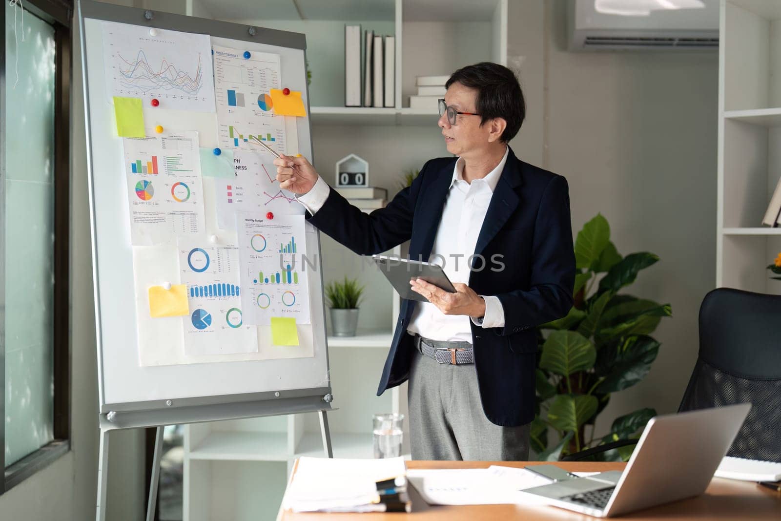 A senior financial advisor reviews budget strategies displayed on charts in a contemporary office, emphasizing analysis and planning.