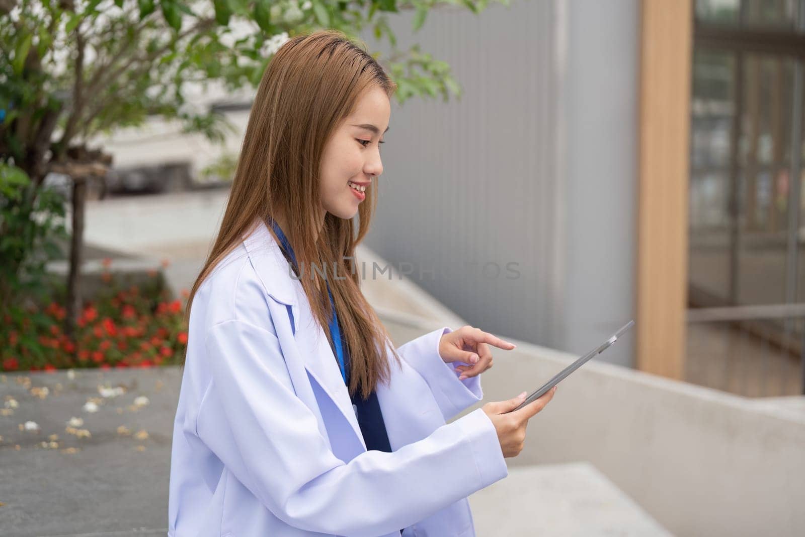 A female doctor in a lab coat uses a tablet outside, illustrating the integration of technology in modern healthcare.
