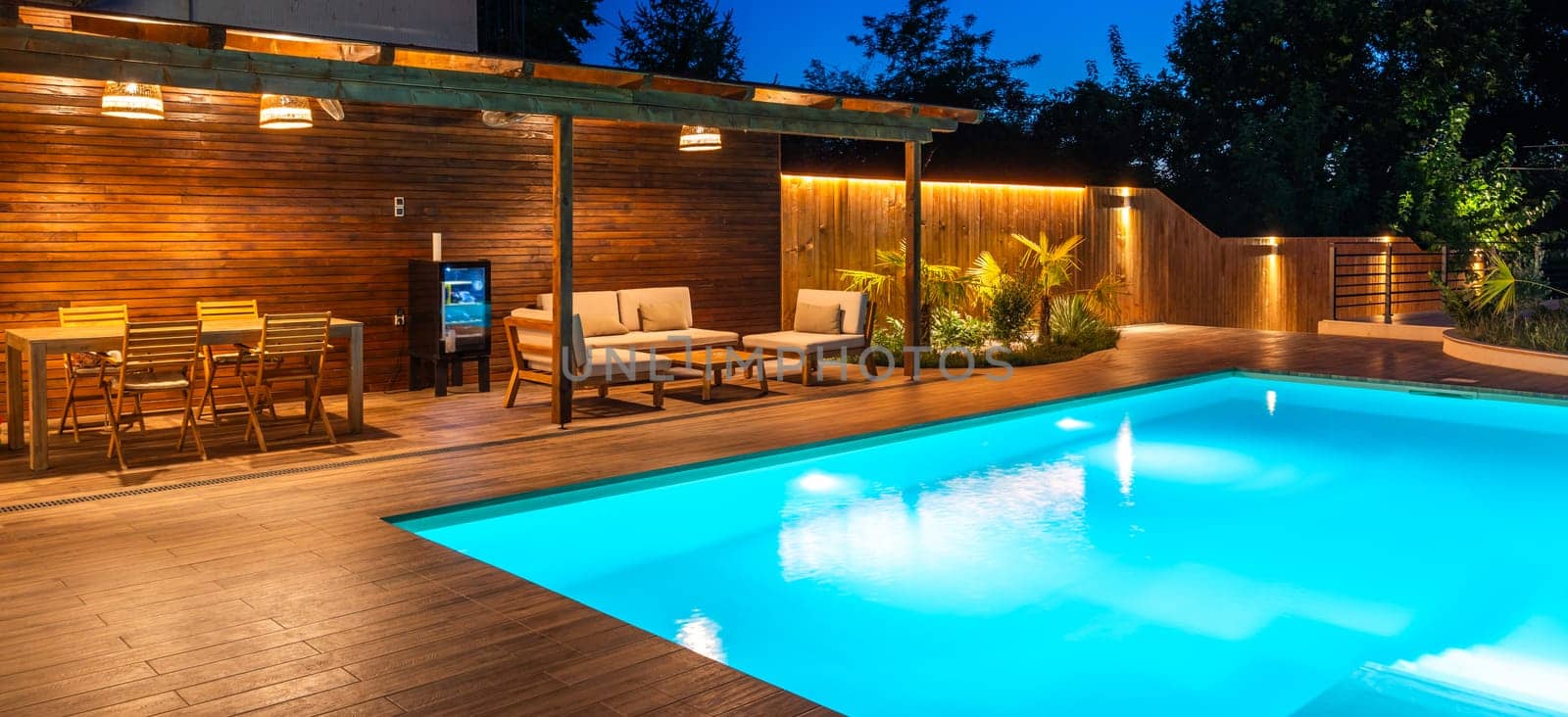 Evening poolside view with dining and lounge area on a wooden deck
