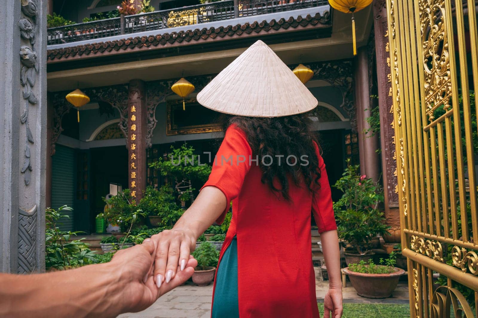 Follow me with back of a female traveler tourist in a Vietnamese hat at a temple in Vietnam in Asia. The concept of travel in Asia