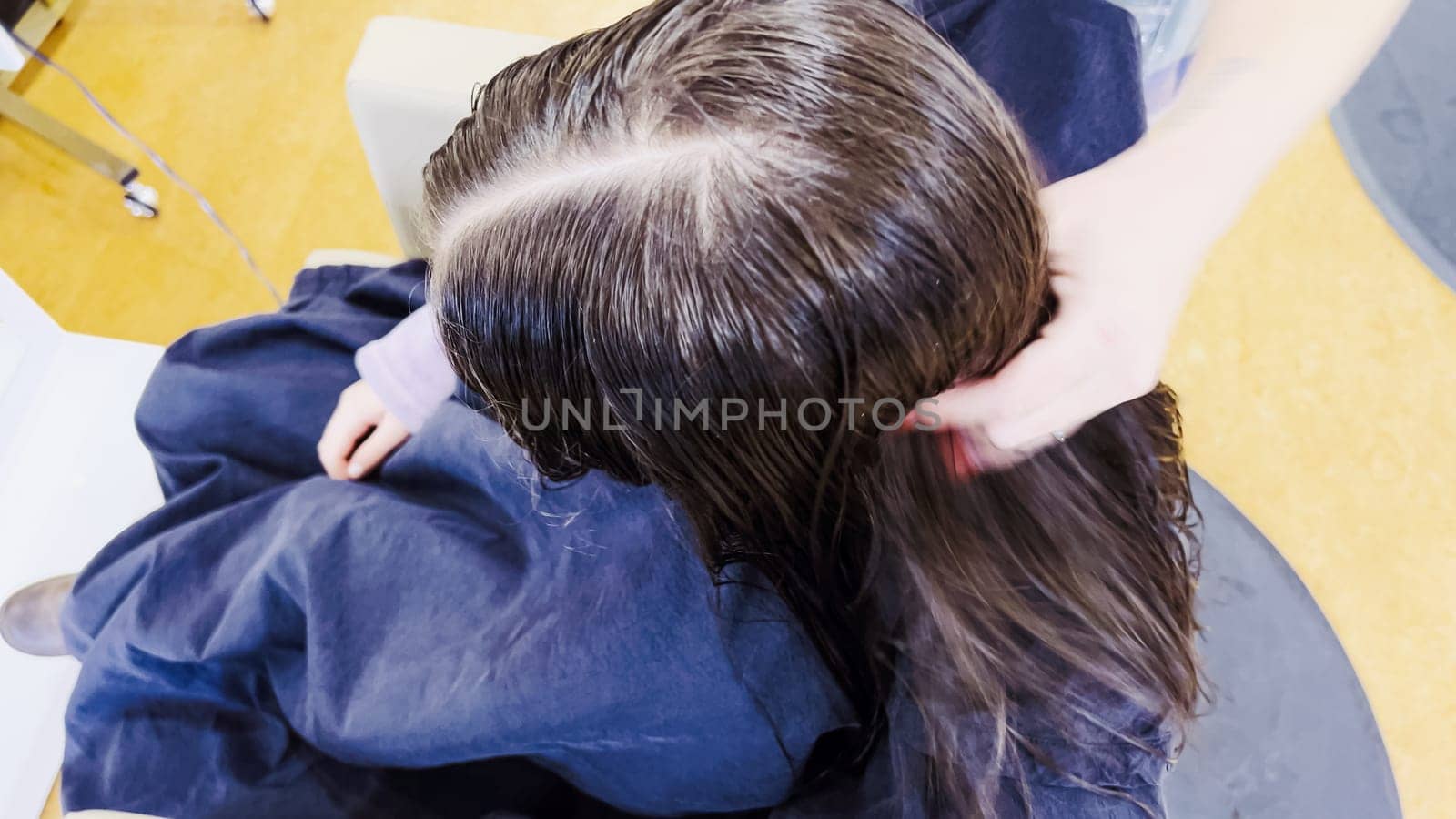 Gentle hands maneuver a hair dryer through a young girl's newly cut hair, showcasing the drying process after a meticulous trim. The warmth of the dryer breathes life into her locks, as they transform from damp to styled with care and expertise.