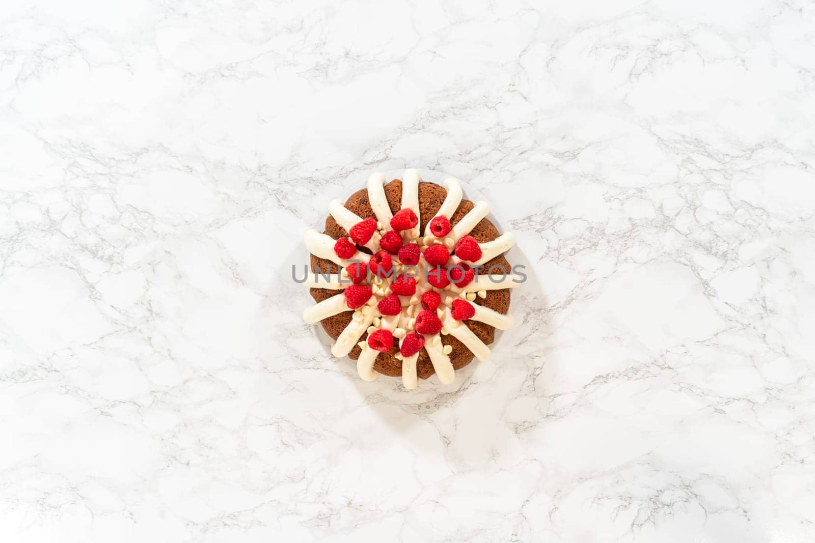 Flat lay. With precision, the White Chocolate Raspberry Bundt Cake is carefully removed from the pan - adorned with luscious cream cheese frosting, creating a delectable treat that is sure to delight.