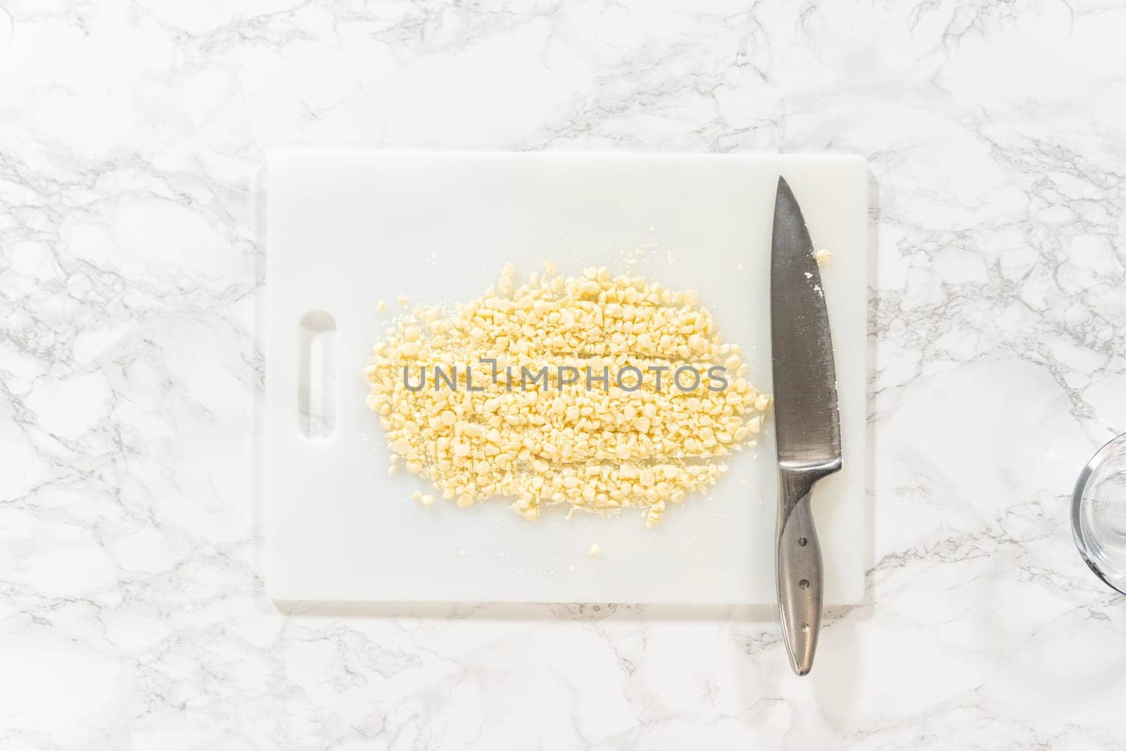 Flat lay. On a white cutting board, skillfully chopping white chocolate chips with a knife adds the perfect touch to a baking adventure.