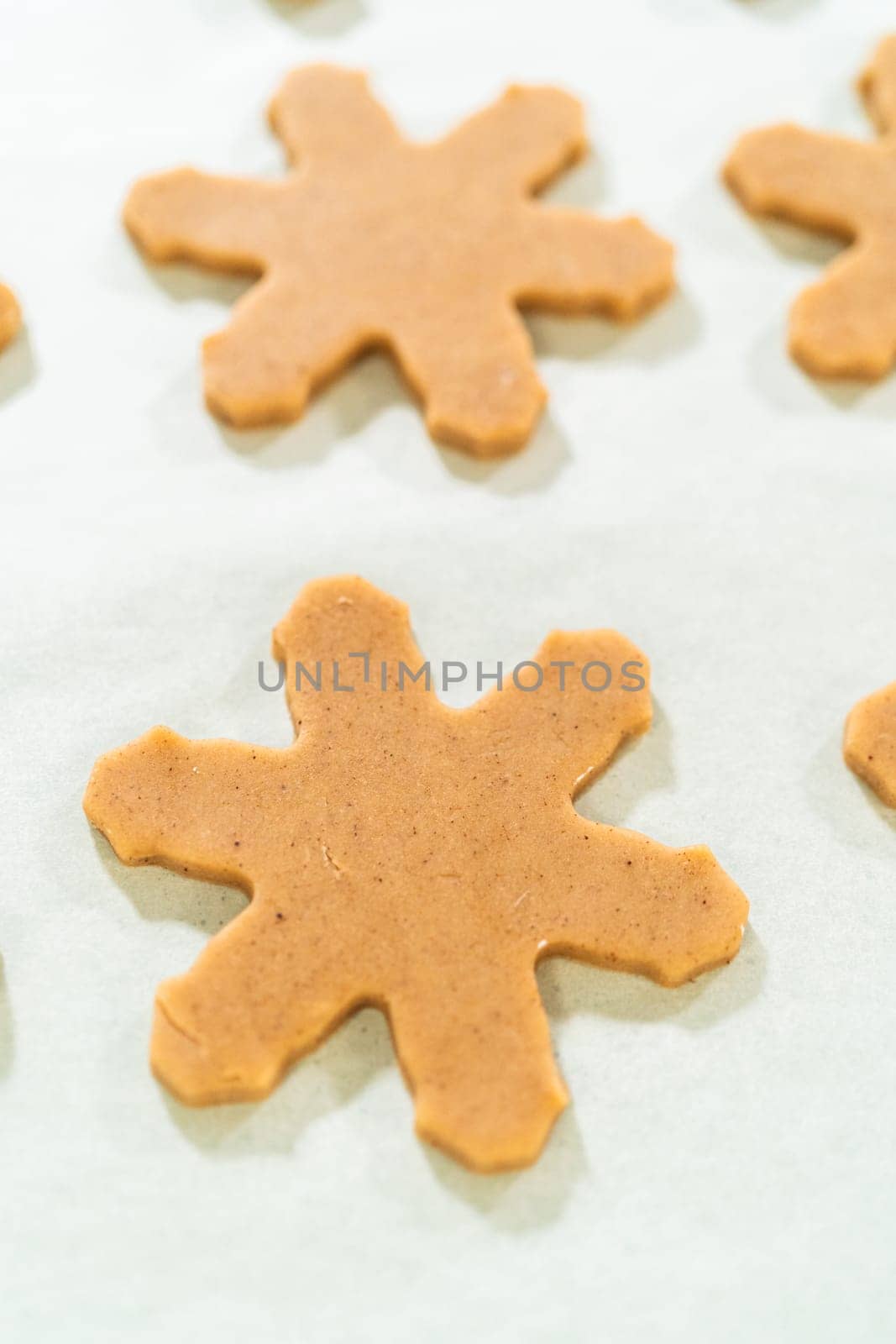 Overhead view of snowflake-shaped amber gingerbread cookie cutouts neatly arranged on a parchment-lined baking sheet during the baking preparation phase.