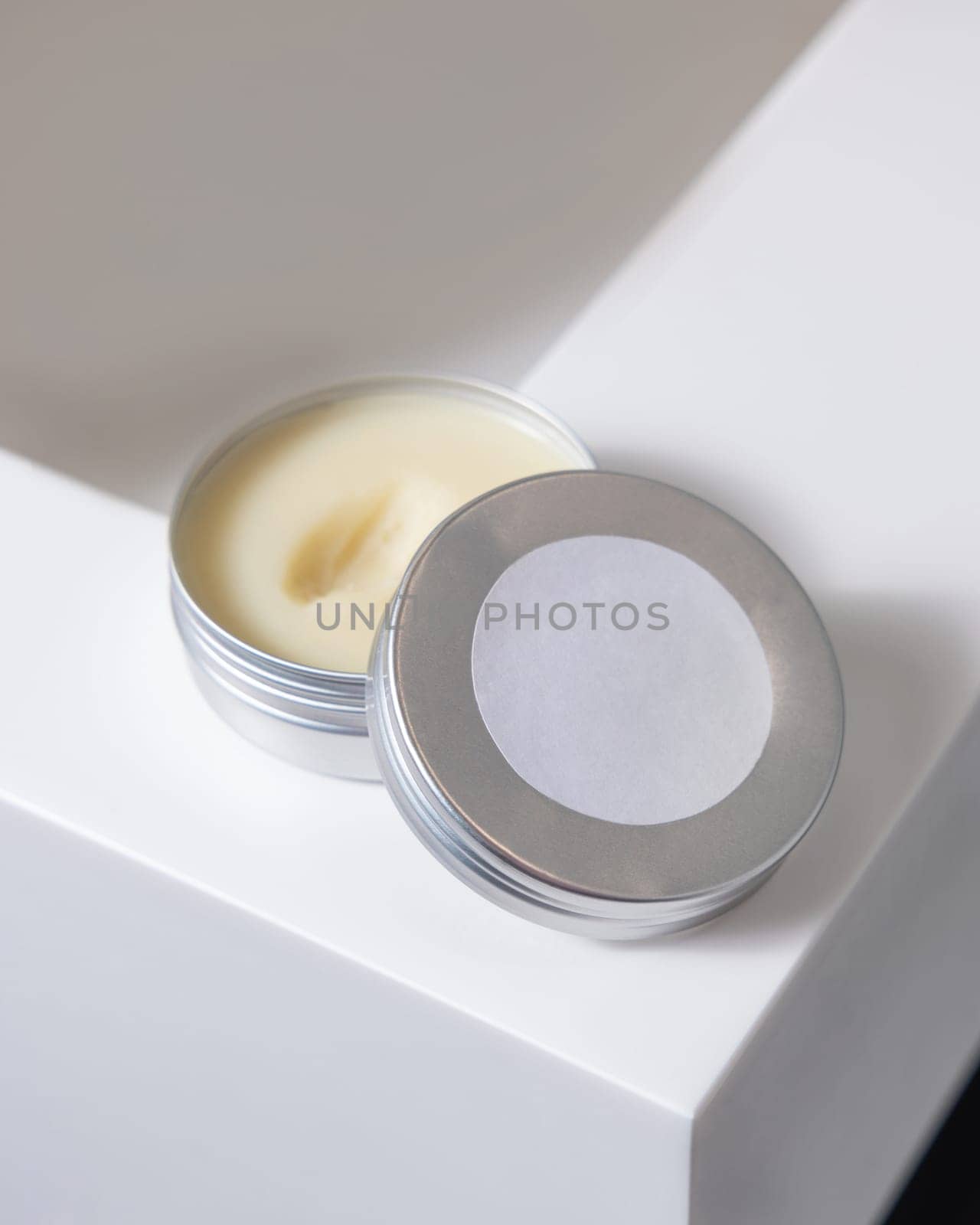Opened body butter jar with blank label on round lid on white washbasin in bathroom, close up. Natural herbal cosmetic product for body care, daily routine or spa procedures