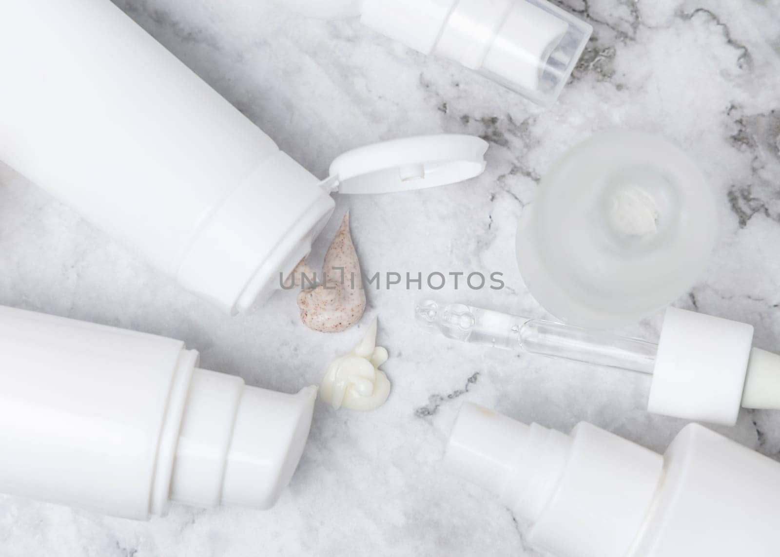 White opened cream tubes, bottles and jars on white marble table top view, mockup. Beige scrub and cream squeezed on table. Natural products for daily face care, spa procedures