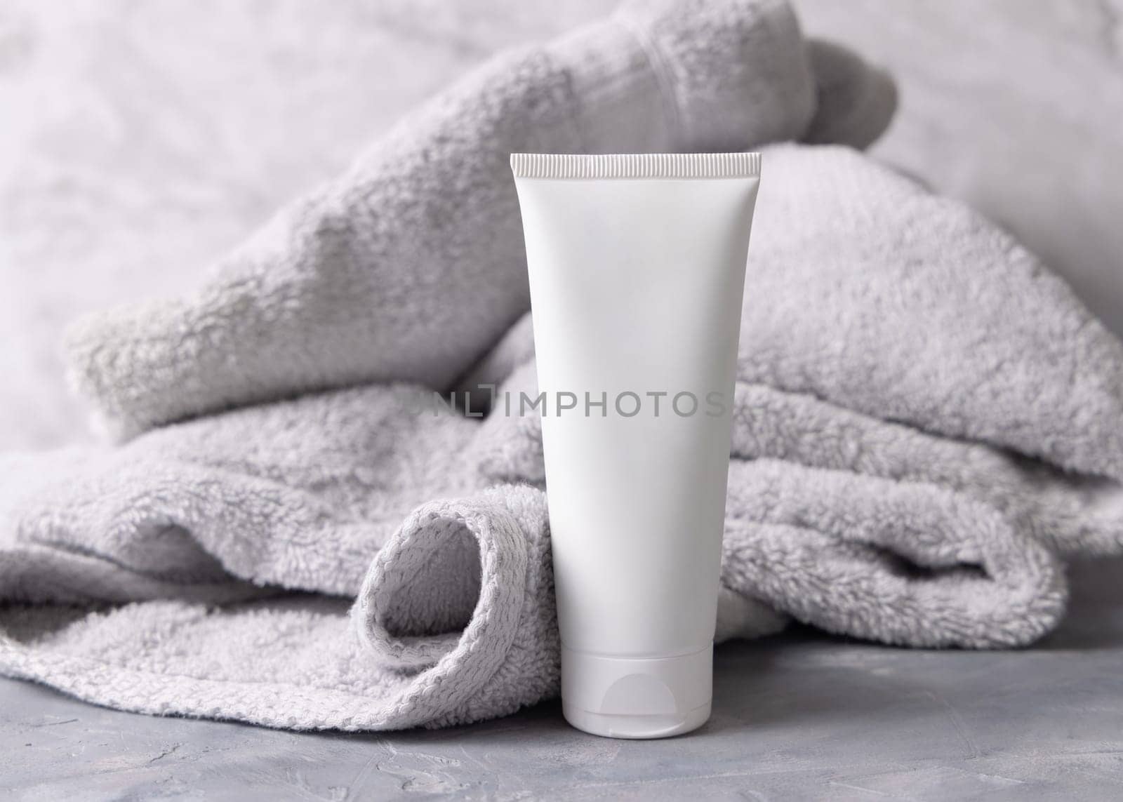White blank cosmetic squeeze cream tube near light grey towel in bathroom top view, brand packaging mockup. Natural herbal cosmetic product for daily facecare, copy space