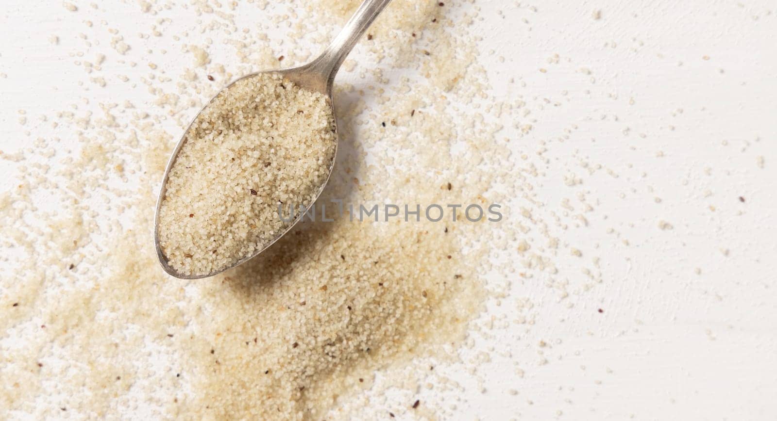 Raw uncooked fonio seeds in a metal spoon on white table top view, copy space. African ancient pseudocereal. Organic super food. Healthy food concept. Gluten free alternative seeds