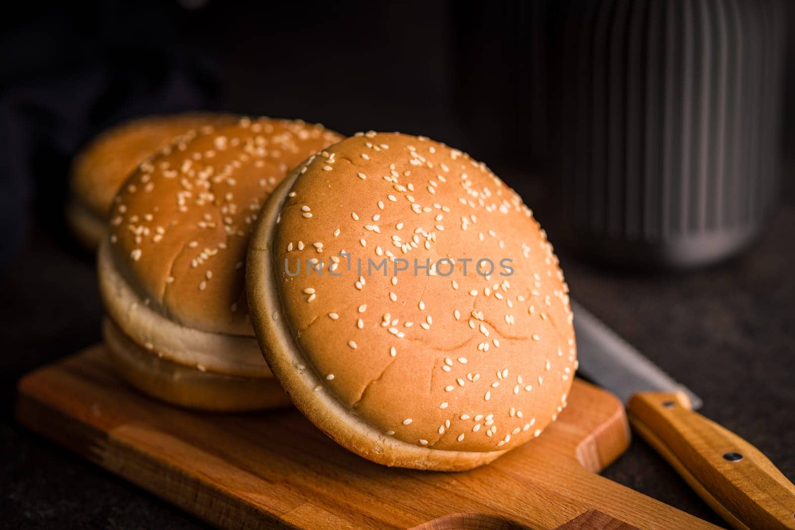 Empty burger bun with sesame seeds on a black table.