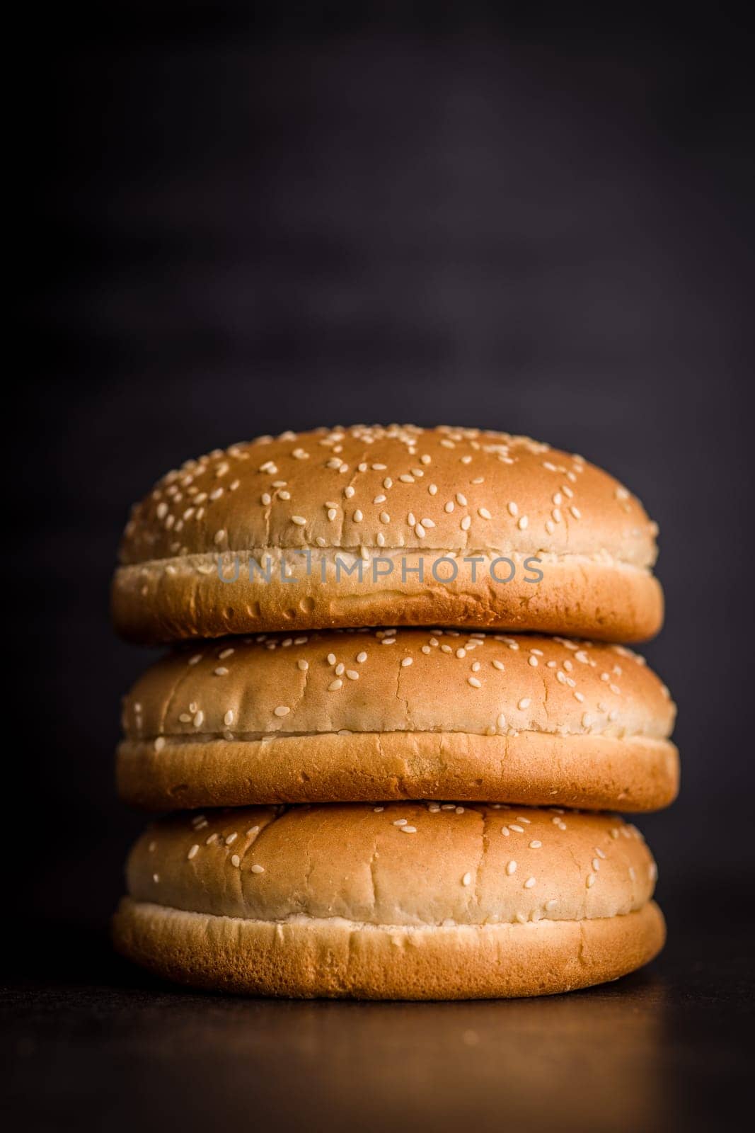 Empty burger bun with sesame seeds on a black table.