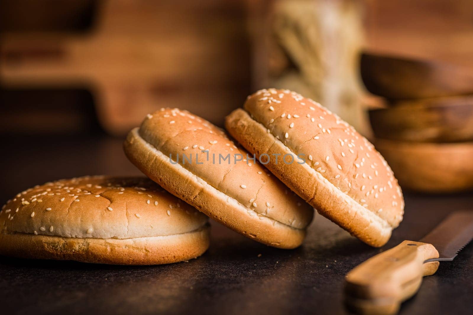 Empty burger bun with sesame seeds on a black table.