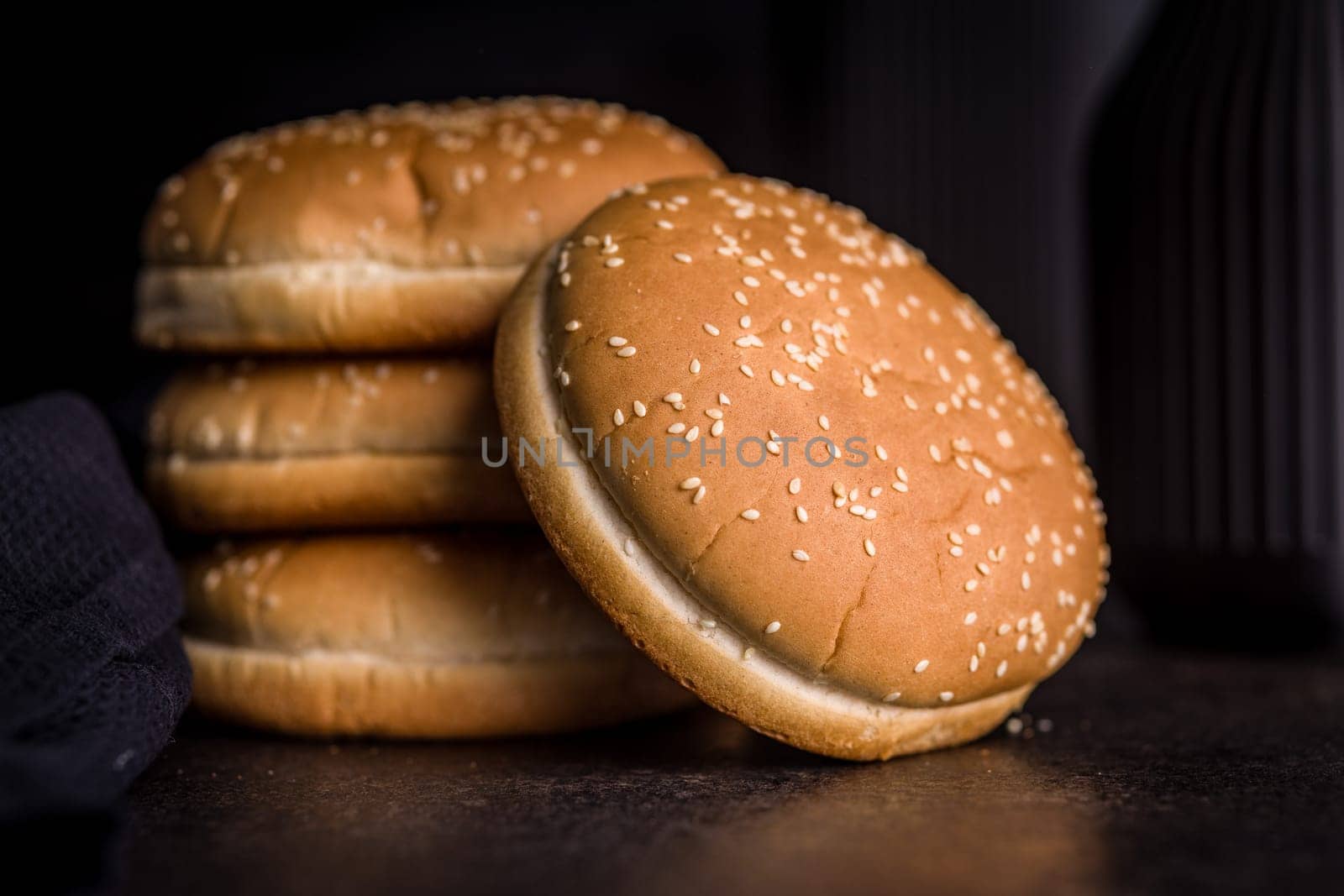 Empty burger bun with sesame seeds on a black table.