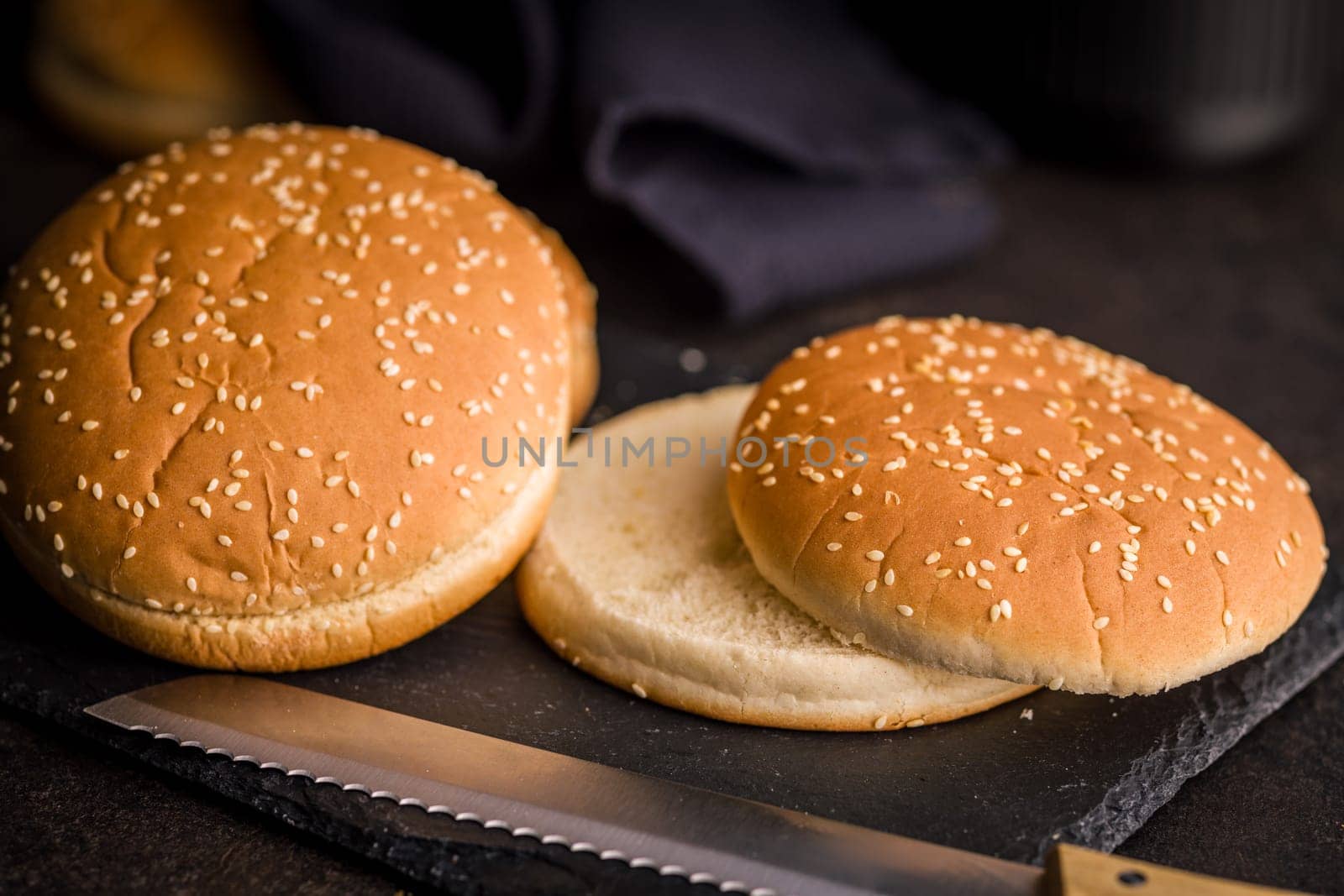 Empty burger bun with sesame seeds on a black table.