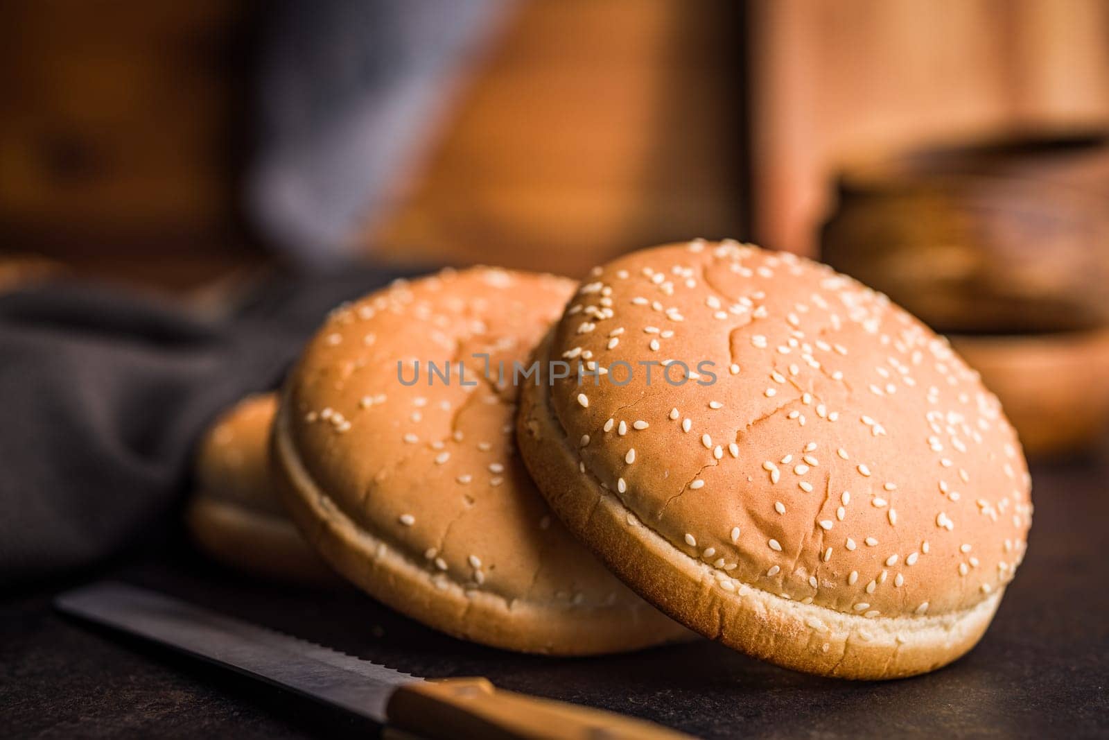 Empty burger bun with sesame seeds on a black table.
