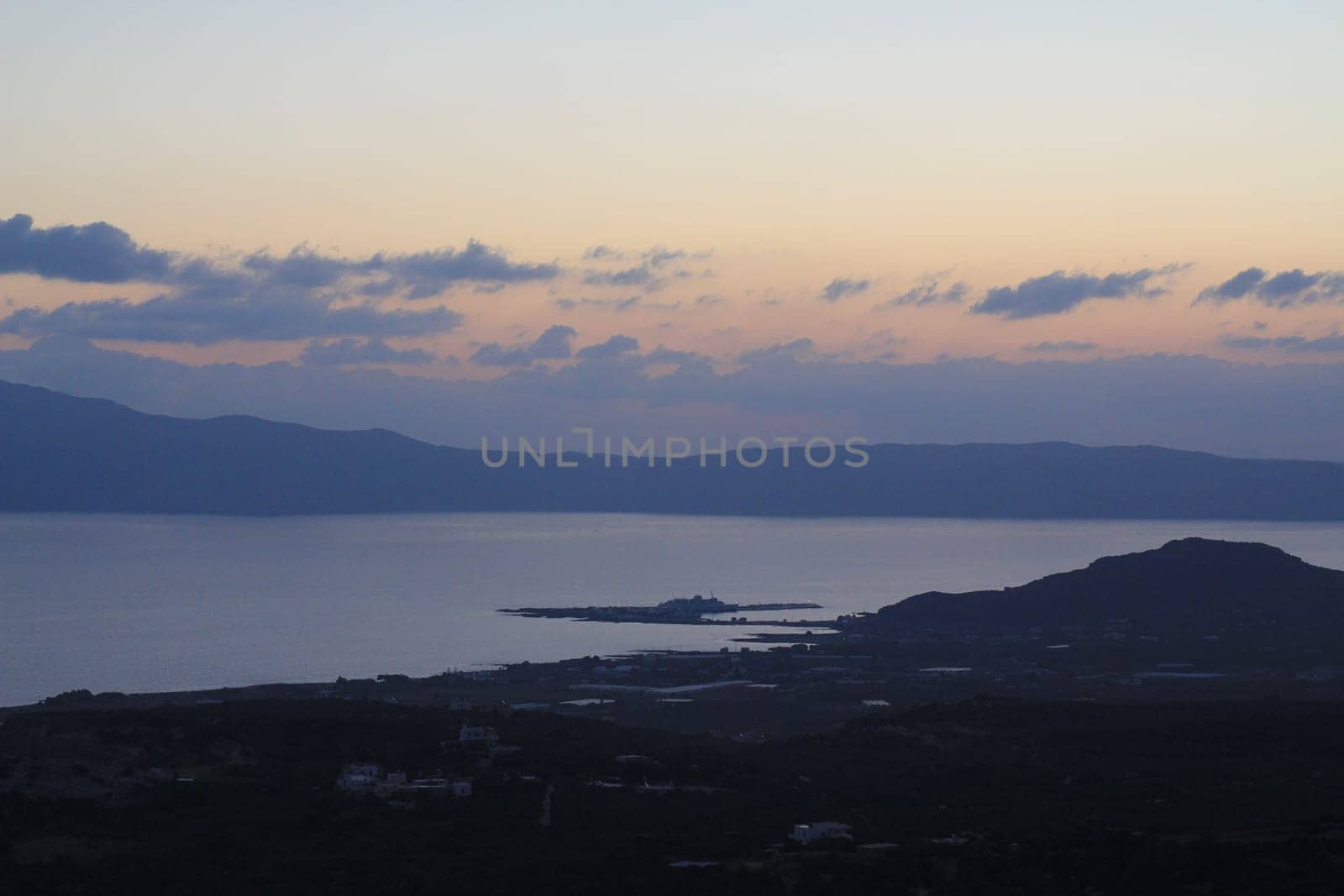The Serene Twilight Casting Its Mystical Glow Over the Calm Sea and Rolling Hills. A beautifully tranquil sunset scene, showcasing serene calm waters reflecting the silhouettes of distant hills