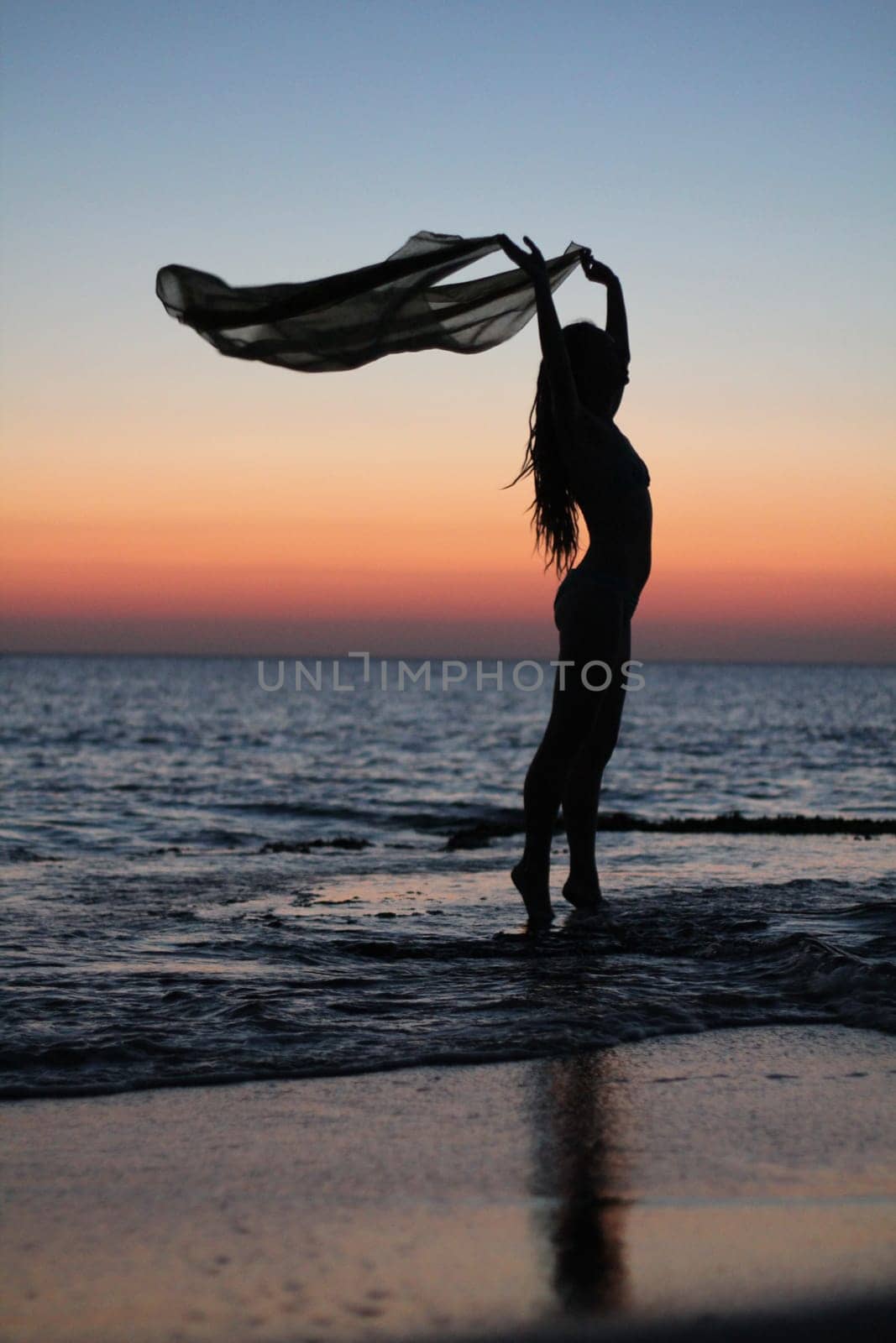 A girl on a beach in Greece during sunset standing on socks and holding a handkerchief in her hands
