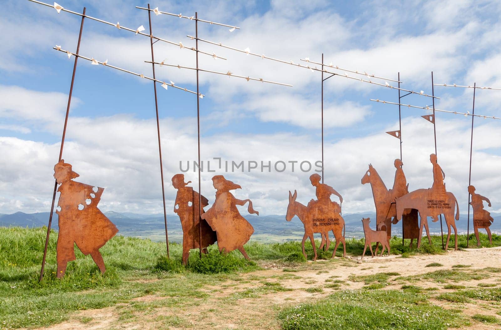 On the Camino de Santiago, metal sculptures of pilgrims walk toward stunning hills under a cloudy sky.
