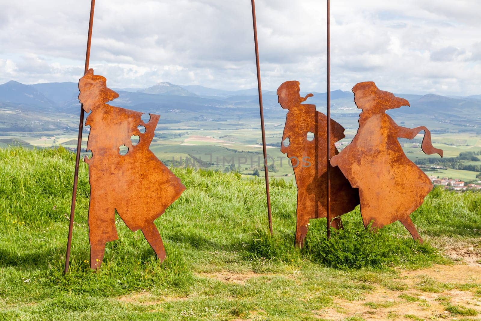 On the Camino de Santiago, metal sculptures of pilgrims walk toward stunning hills under a cloudy sky.