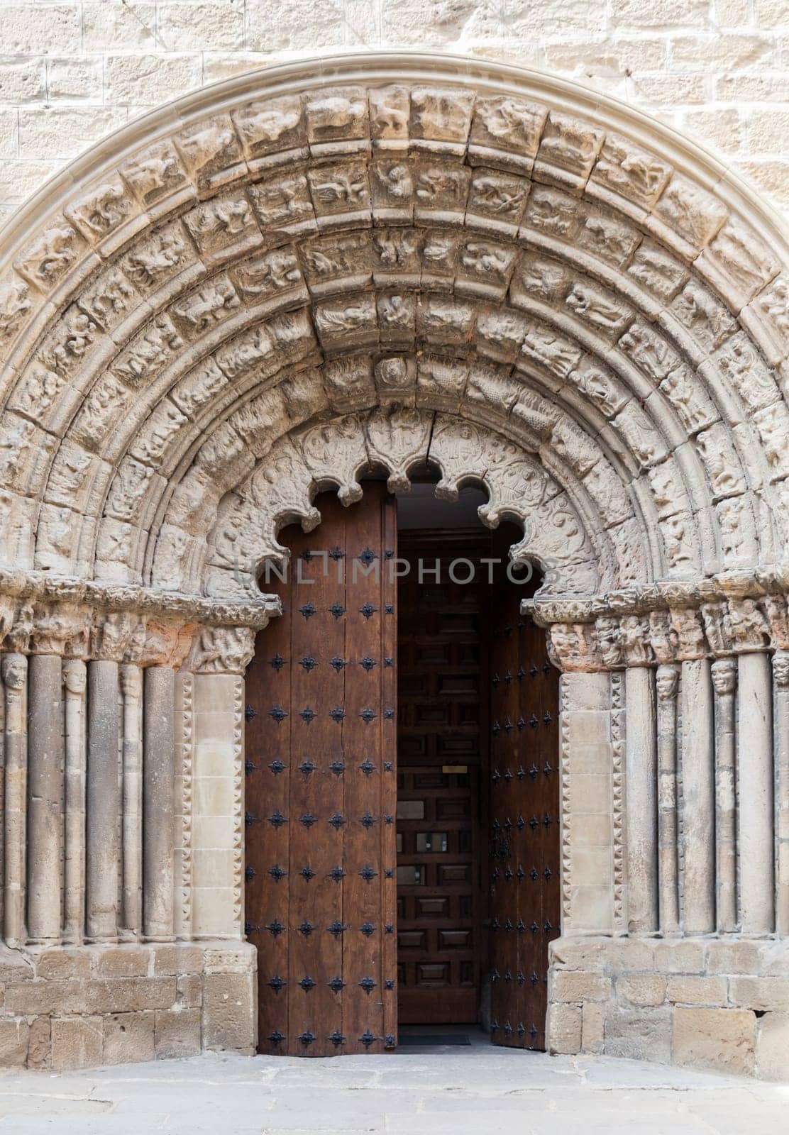 A beautifully carved stone archway frames the large wooden doors of an ancient church in Obanos, showcasing intricate craftsmanship.