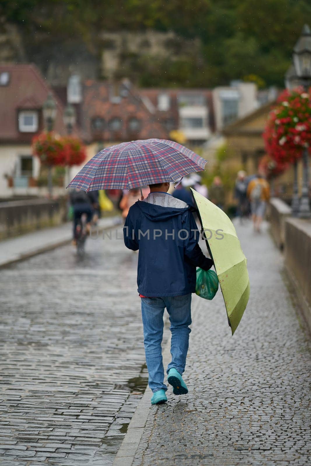 Wuerzburg, Germany – September 26, 2024: Asian tourist with two umbrellas in rainy weather on the old Main bridge, alte Mainbrücke in Wuerzburg