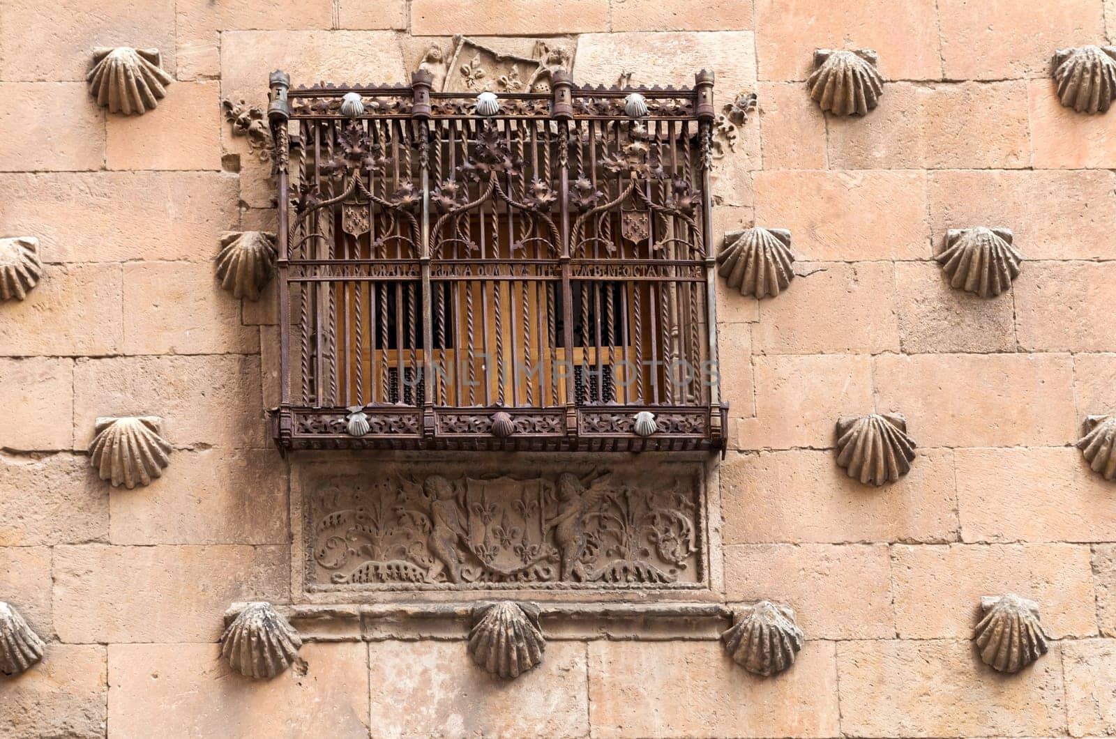 A detailed view of a historic stone building in Salamanca, featuring a decorative window with intricate ironwork.