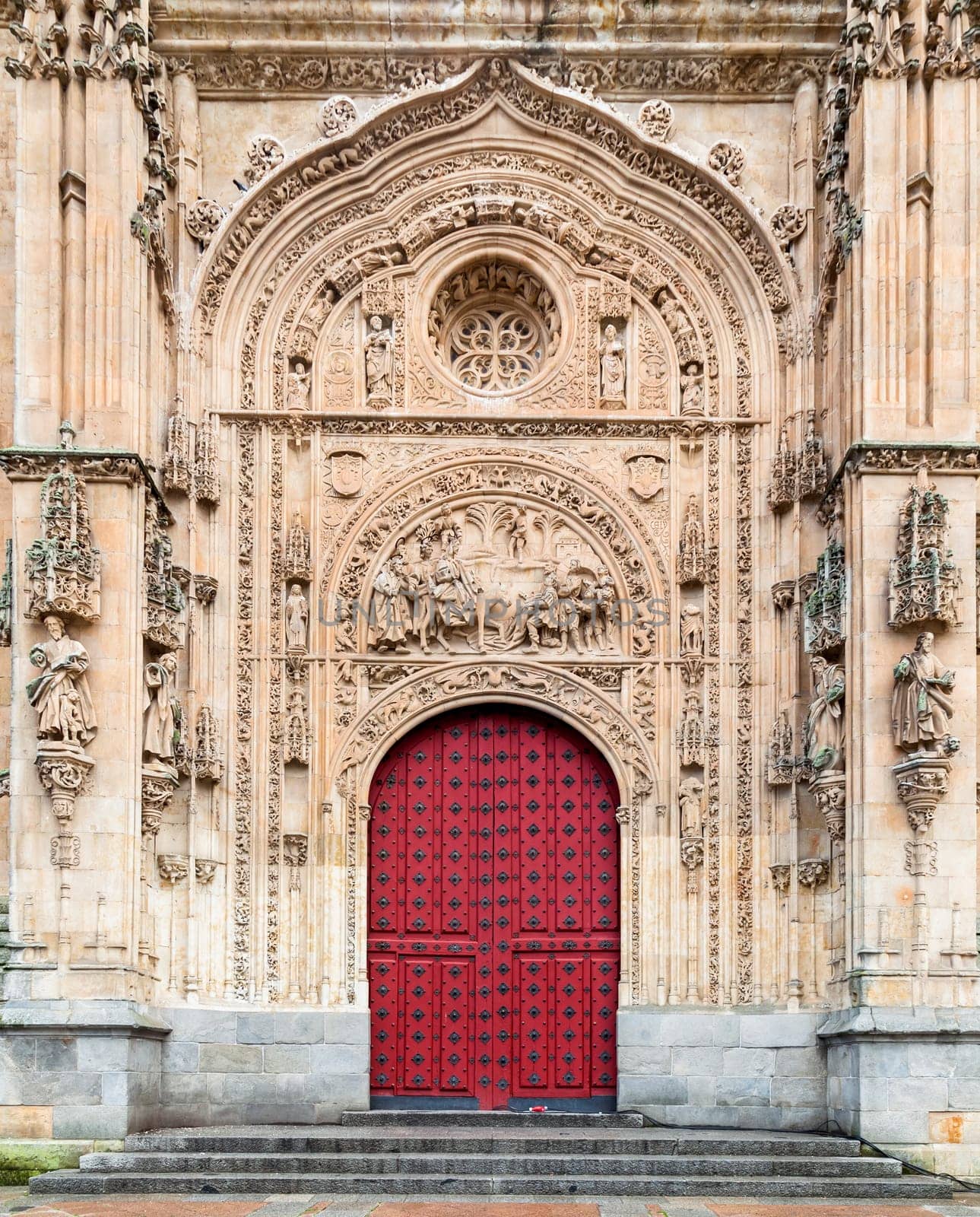 The ornate entrance of Salamanca Cathedral features intricate carvings and a striking red door, highlighting its architectural beauty.