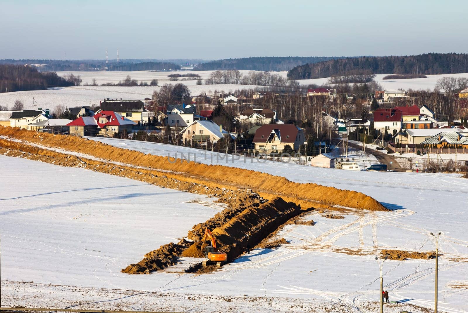 Road construction. Excavator digs a trench for laying a sewer pipe on a cloudy winter day. Selective focus, shallow depth of field, engineering works in the village in winter