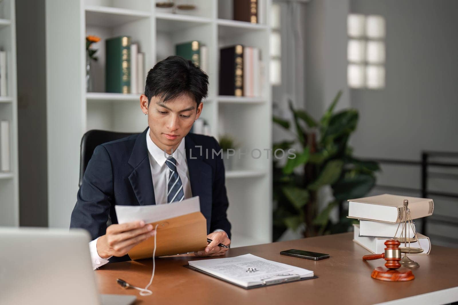 A young businessman is focused on reviewing important documents while holding an envelope, showcasing professionalism in a contemporary office environment.