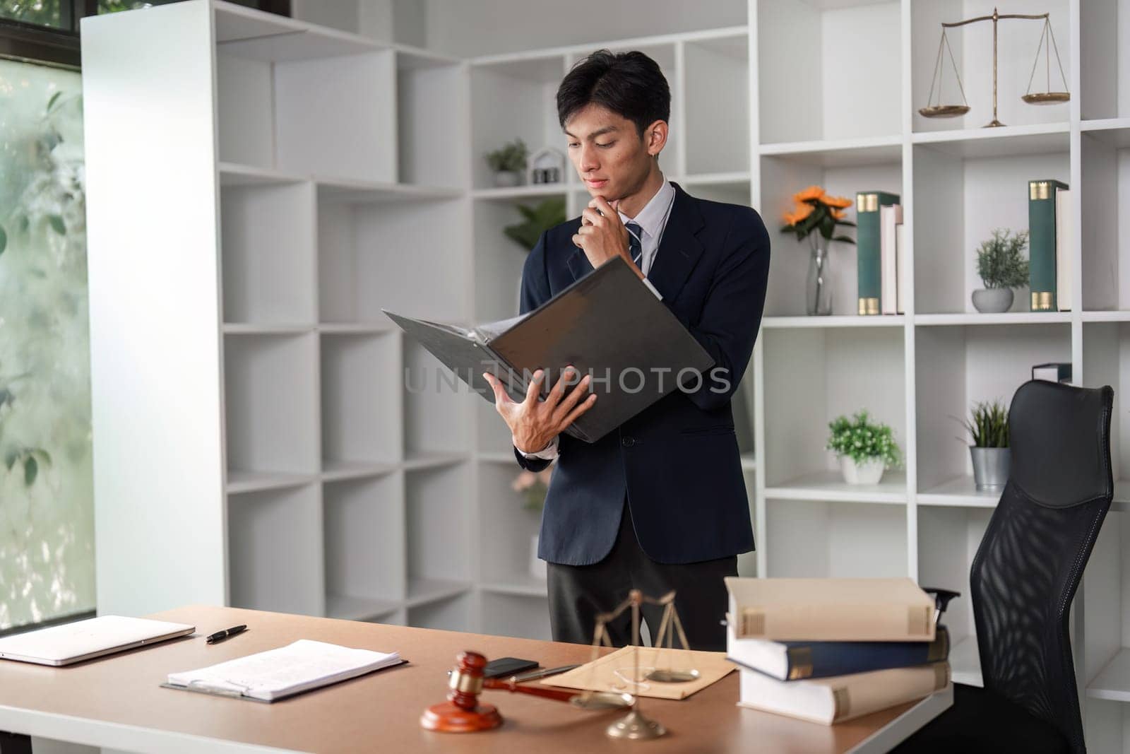 A thoughtful young Asian lawyer is analyzing case files and legal documents in a modern office setting, contemplating legal strategies.