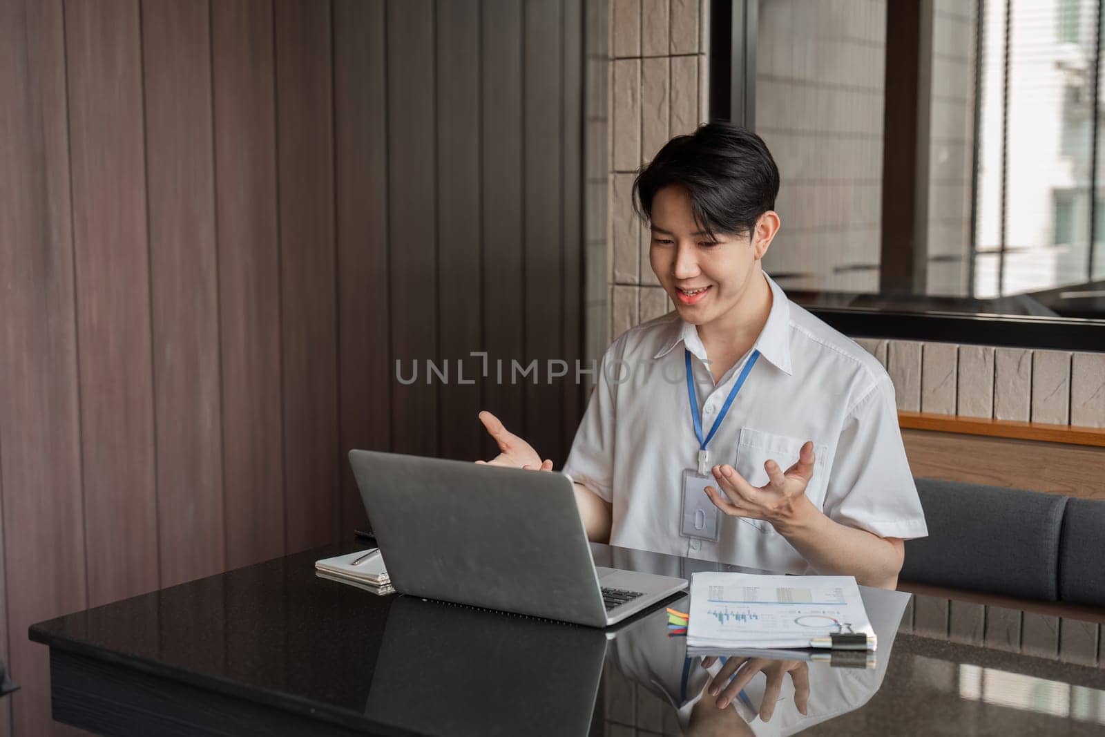 An engaged young professional is animatedly expressing his ideas during a video call on his laptop in a sleek office, enhancing teamwork and collaboration.