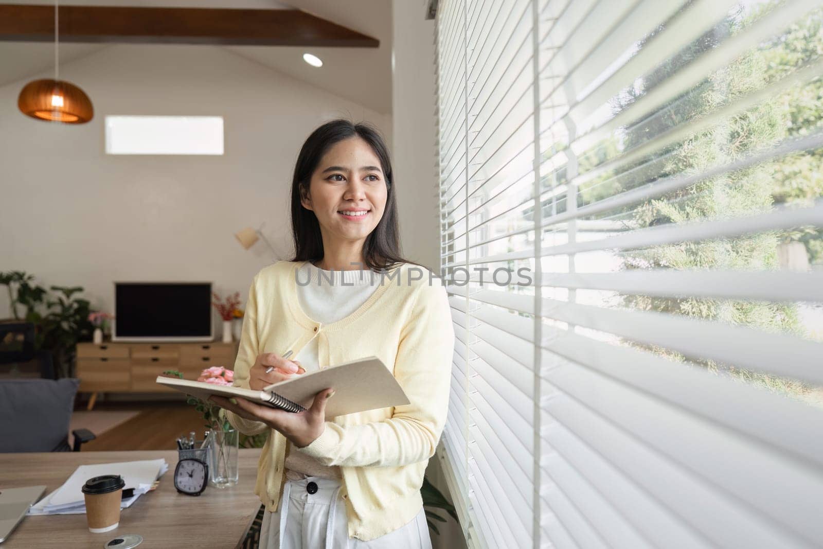 A focused woman in a cozy home office writes in her notebook, showcasing a blend of productivity and comfort.