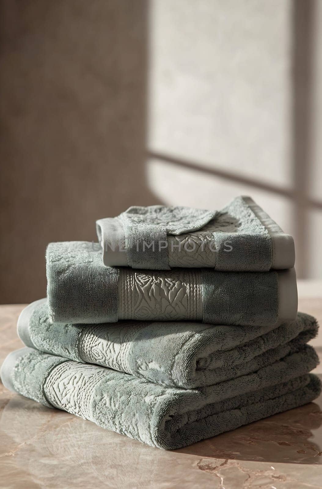 Plush green towels are neatly stacked on a marble surface, illuminated by natural light from a nearby window, creating a serene atmosphere.