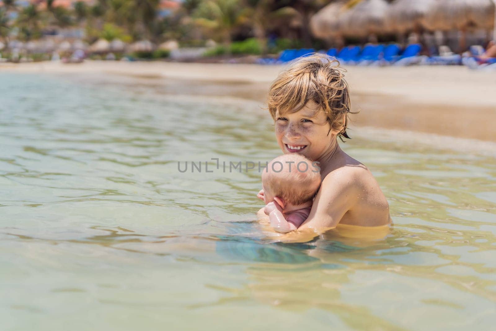 An older brother gently holds his baby sibling while swimming in the sea, sharing a joyful and heartwarming moment of family bonding and summer fun in the water. A perfect blend of love, care, and childhood adventure.