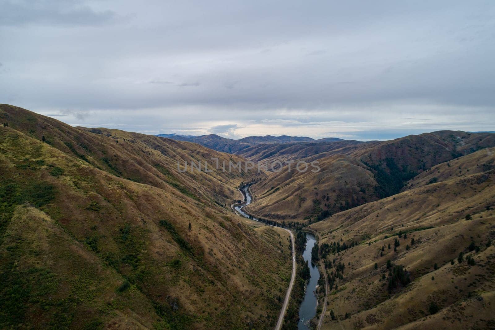 A mountain range with a river running through it. The sky is cloudy, and the landscape is mostly brown and green. Scene is peaceful and serene, with the river