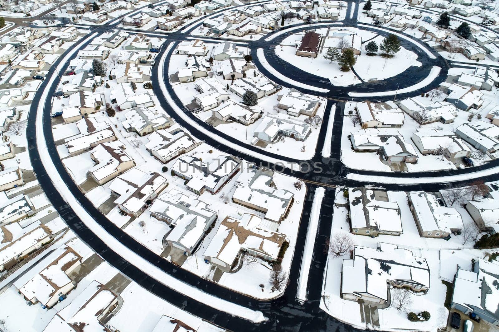 A snow covered neighborhood with houses and a round street. The houses are all small and the street is surrounded by snow