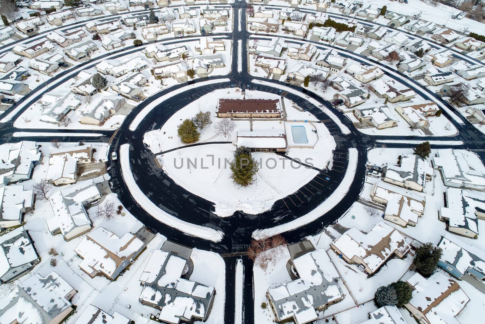 A snow covered neighborhood with a large circle in the middle. The circle is surrounded by houses and a pool