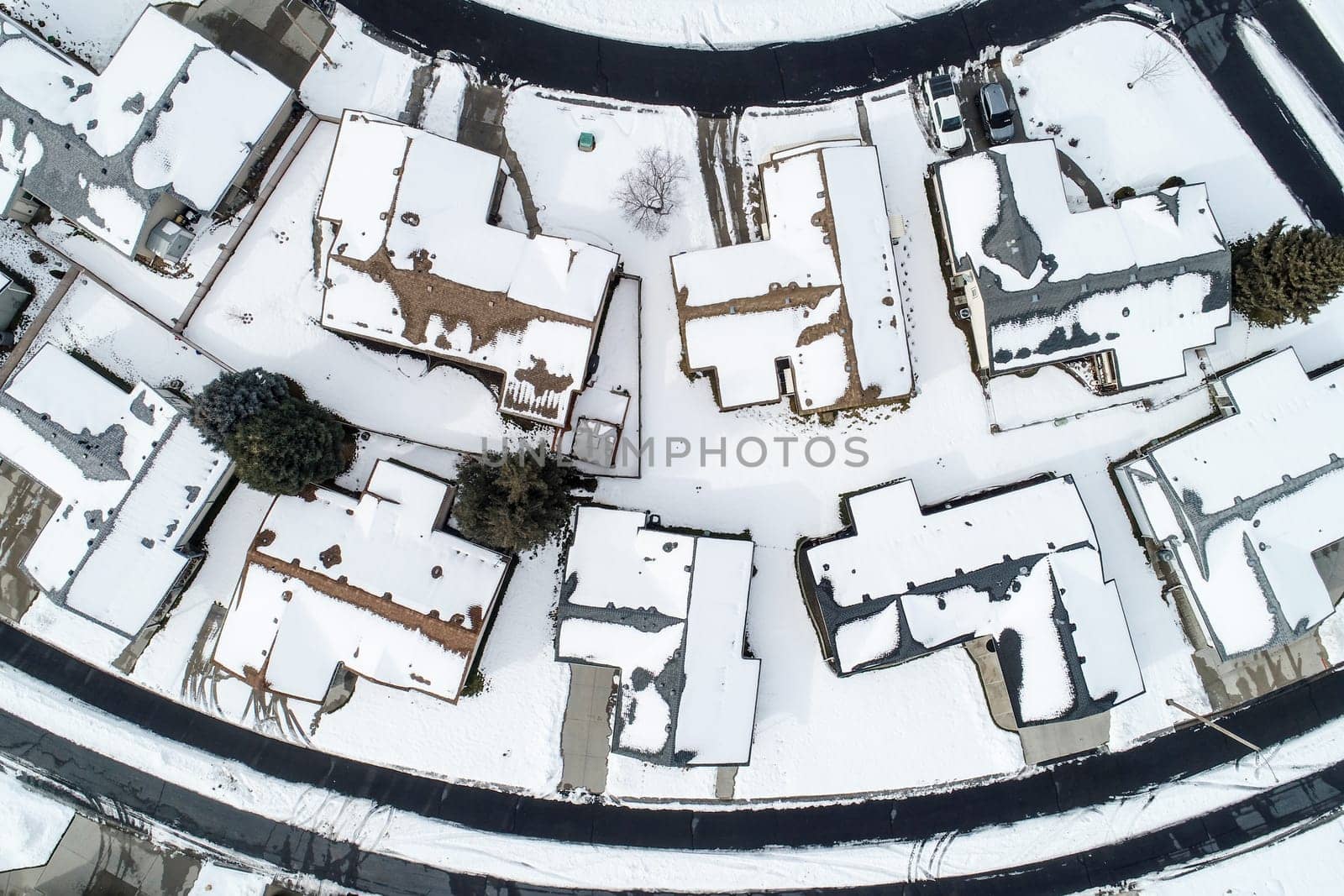 A snow covered neighborhood with houses and a street. The houses are all lined up in a row and the street is empty