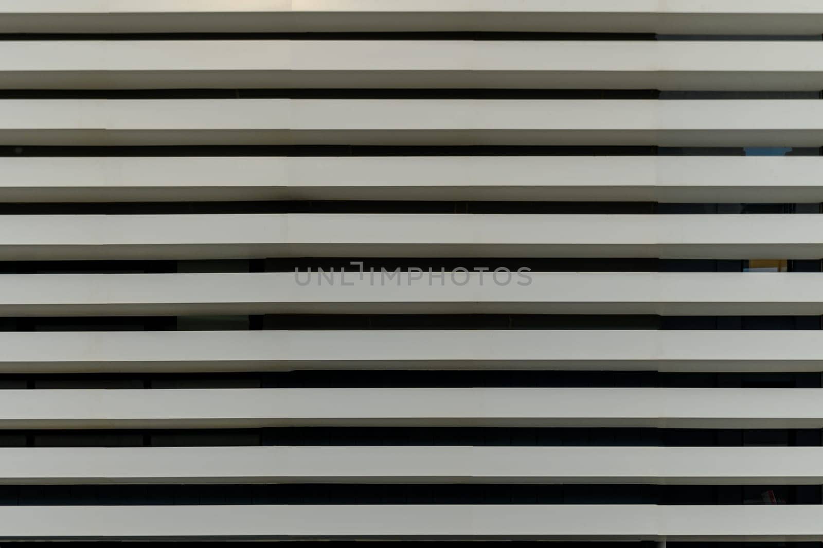 Vertical lines converge as sleek white slats create a rhythmic pattern on a modern urban structure during daylight.
