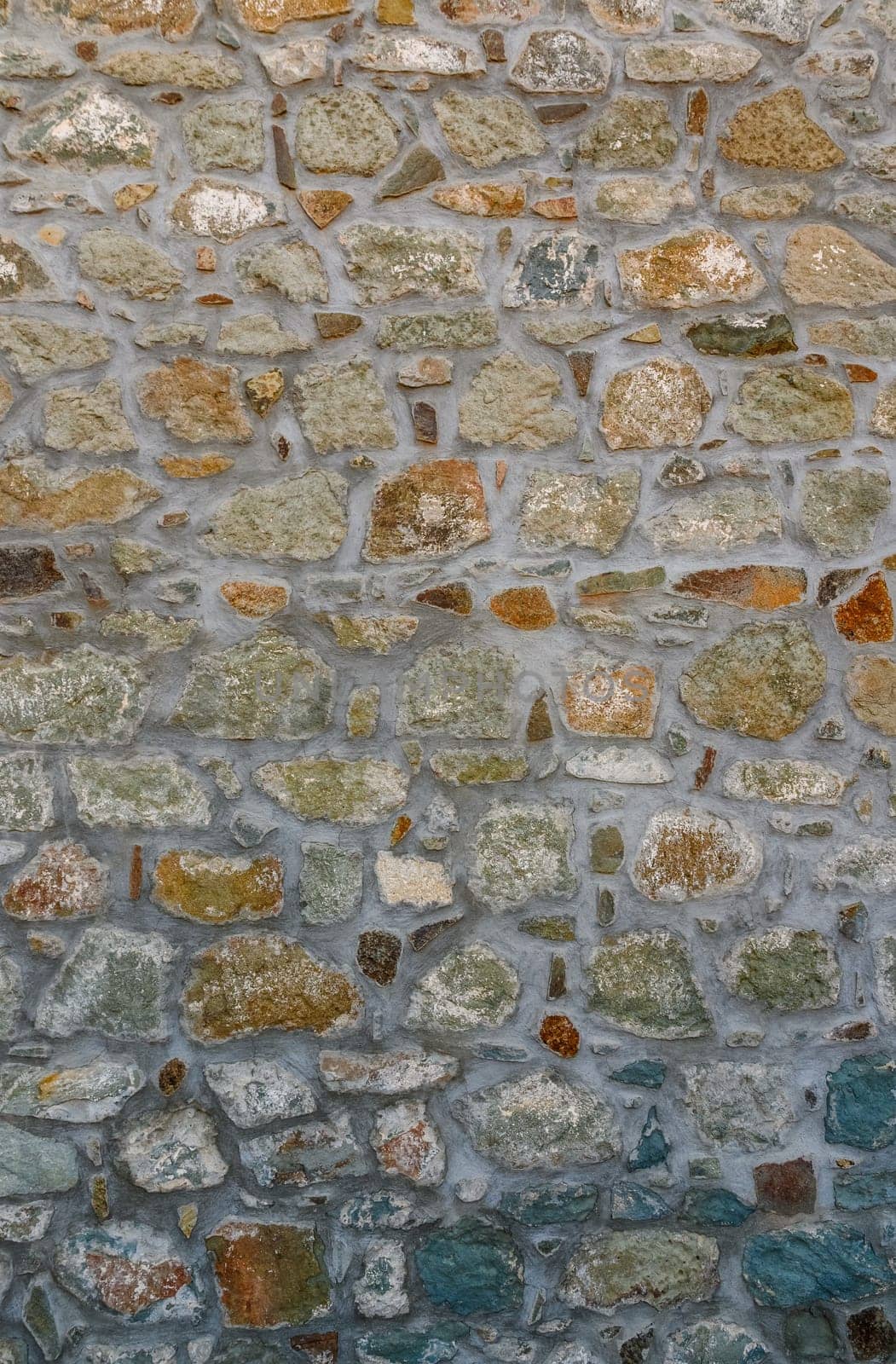 Rugged stone wall displays a stunning mosaic of colors, illuminated by warm sunlight on a clear day.