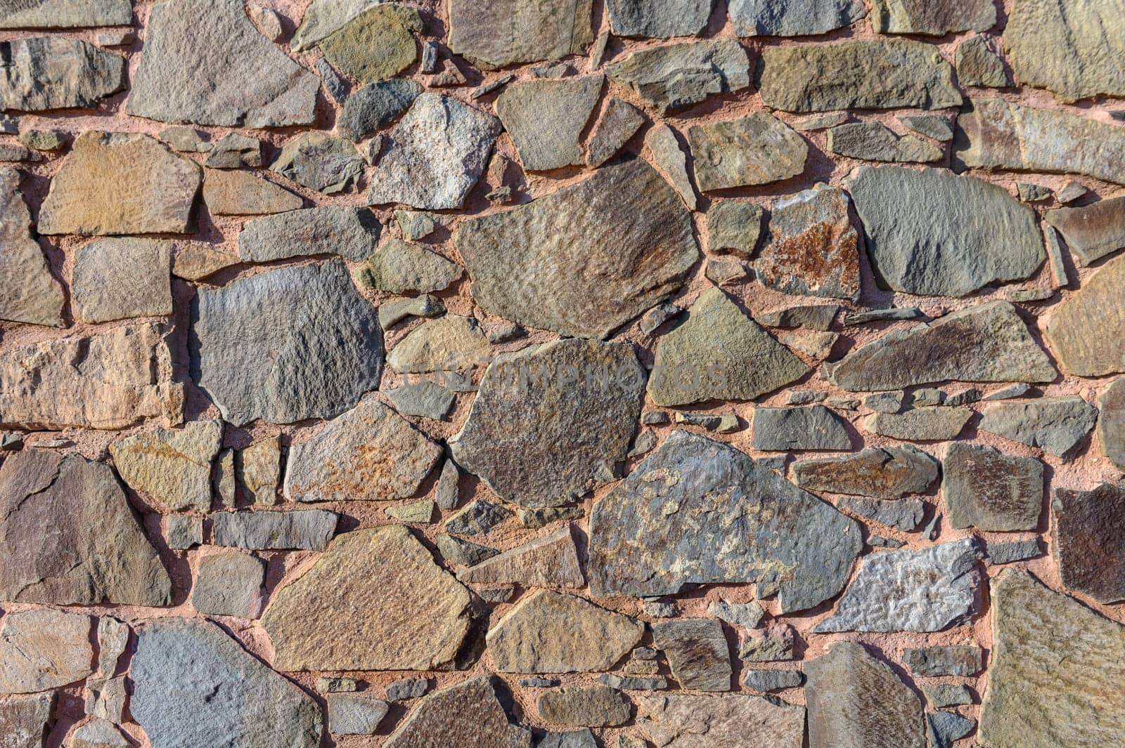 Stones of various shapes and shades create a textured facade, basking in warm sunlight on a quiet day.