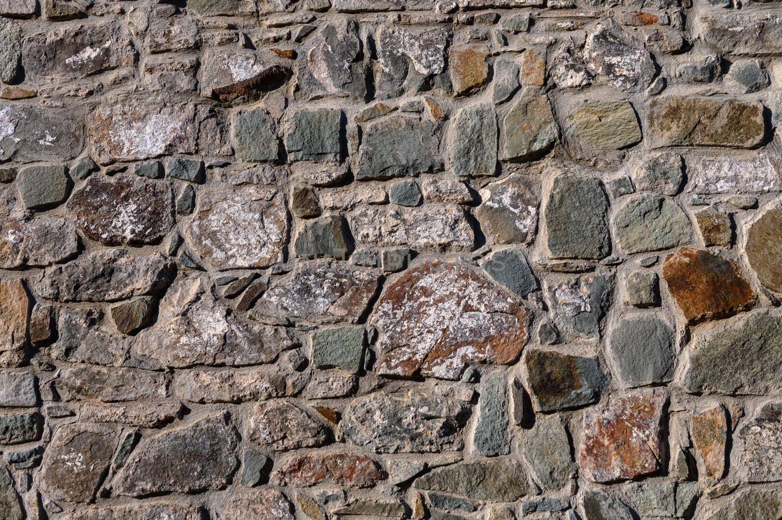 Rough stones form a captivating wall, displaying rich textures and hues under warm sunlight at a historic location.