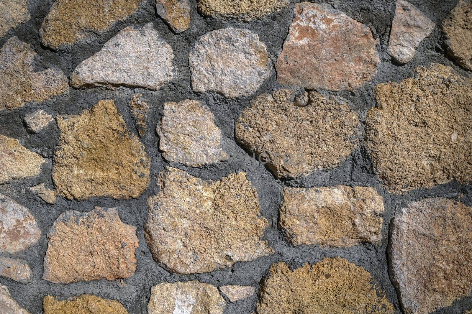 Natural stones fill the rustic wall, enhancing the charm and texture in the sunlit outdoor space.
