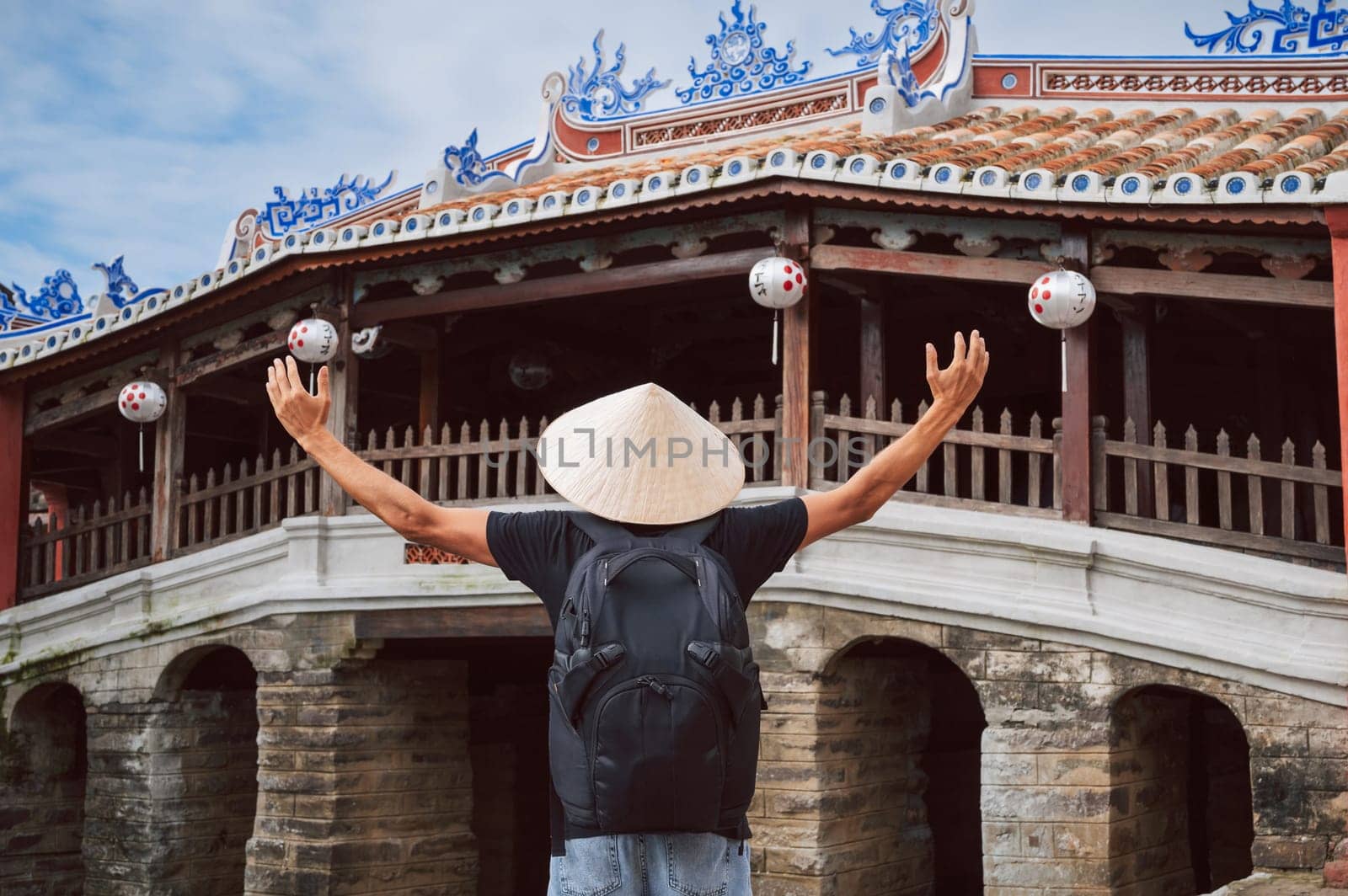 back of male traveler tourist in a Vietnamese hat at the ancient Japanese covered bridge in old town in Hoi An in Vietnam in Asia