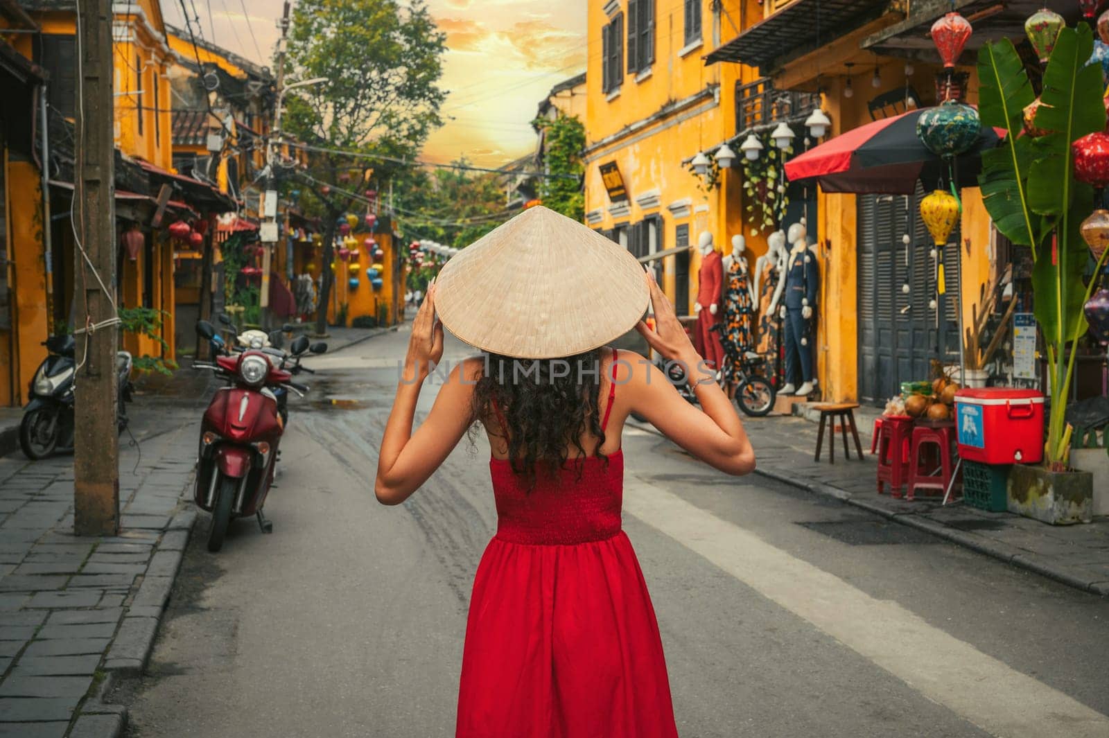 back of beautiful woman tourist in traditional Vietnamese hat and red dress on street in old town in Hoi An city in Vietnam in Asia
