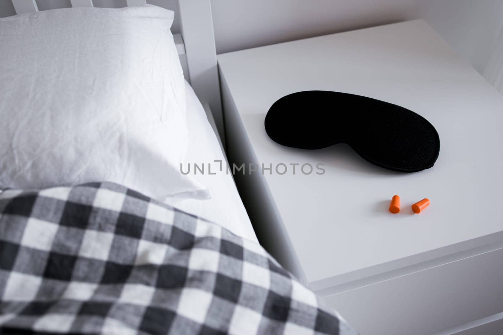 Cozy bedside scene with sleep mask and earplugs on white nightstand.