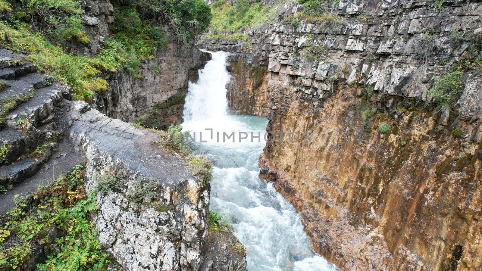 Stunning waterfall cascading down into a narrow canyon, featuring intricately carved stone steps along the side, creating a breathtaking display of nature's beauty and power