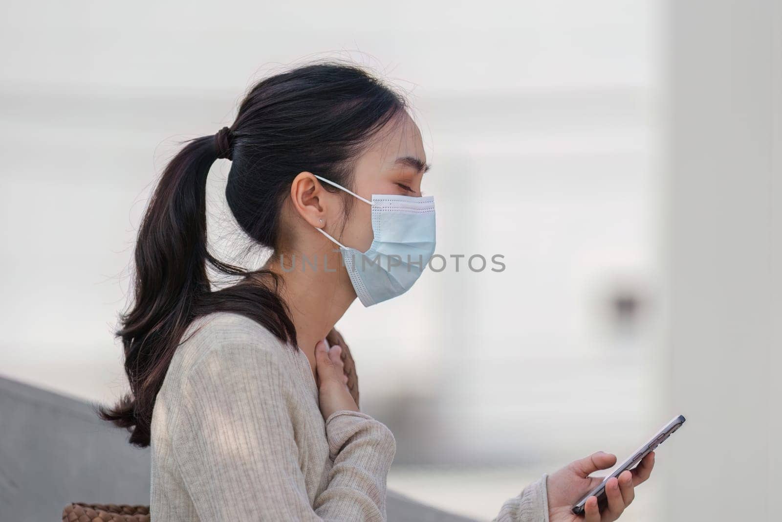 A young woman wearing a face mask checks her phone outdoors, reflecting health awareness in response to pollution.