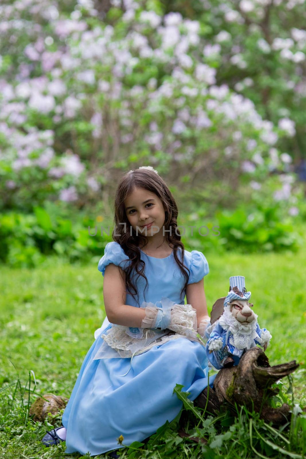Young caucasian girl in blue dress with toy rabbit in lilac garden