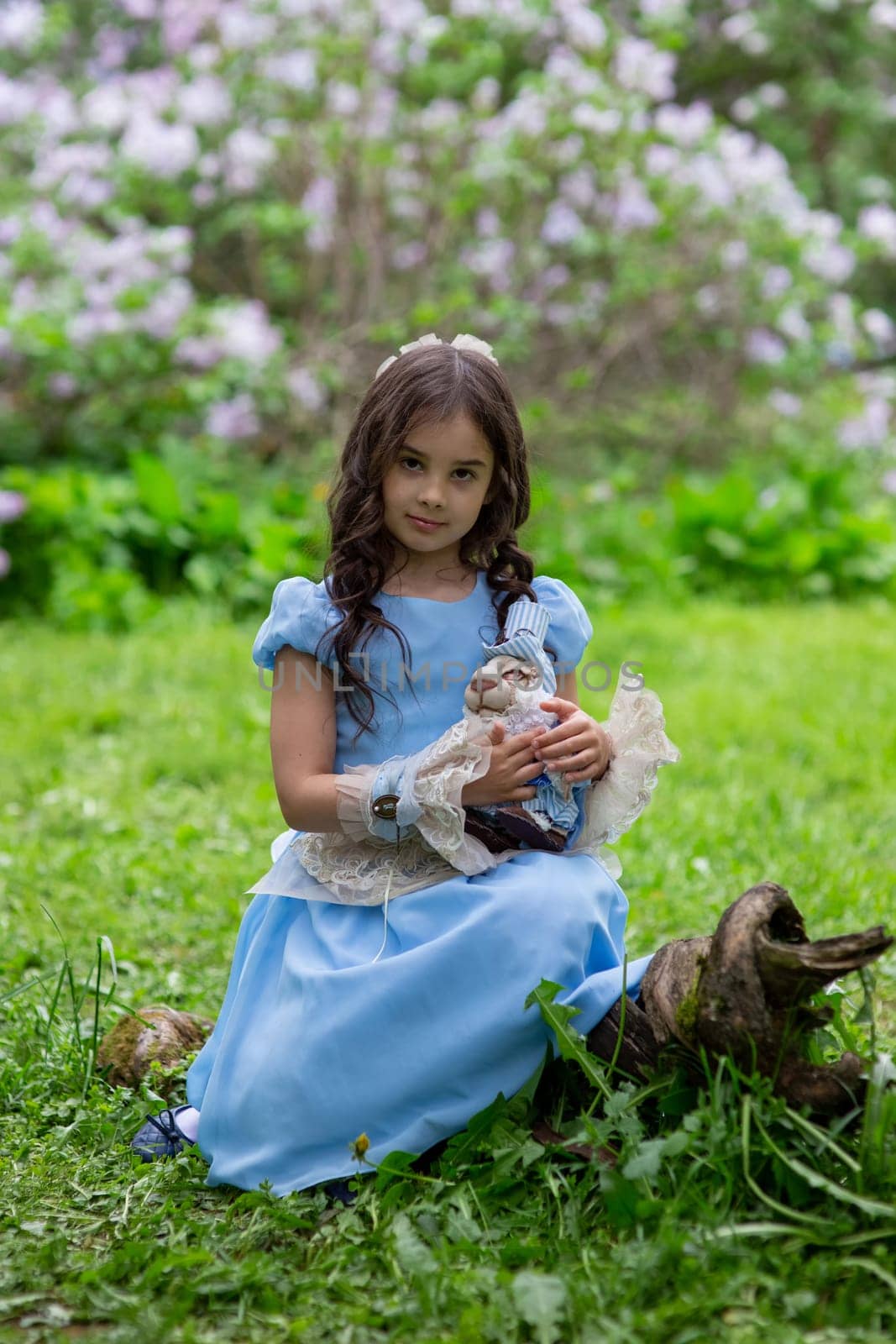 Young caucasian girl in blue dress holding doll in garden setting.